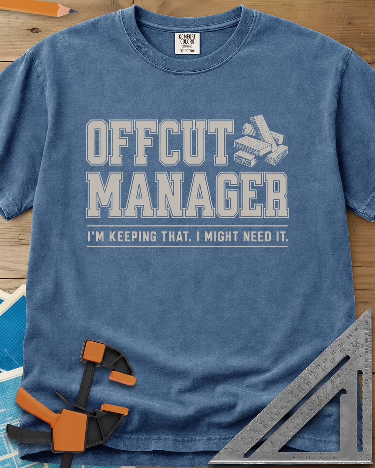 Offcut Manager heavyweight tee in Blue Jean, varsity block lettering beside a little stack of wood offcuts