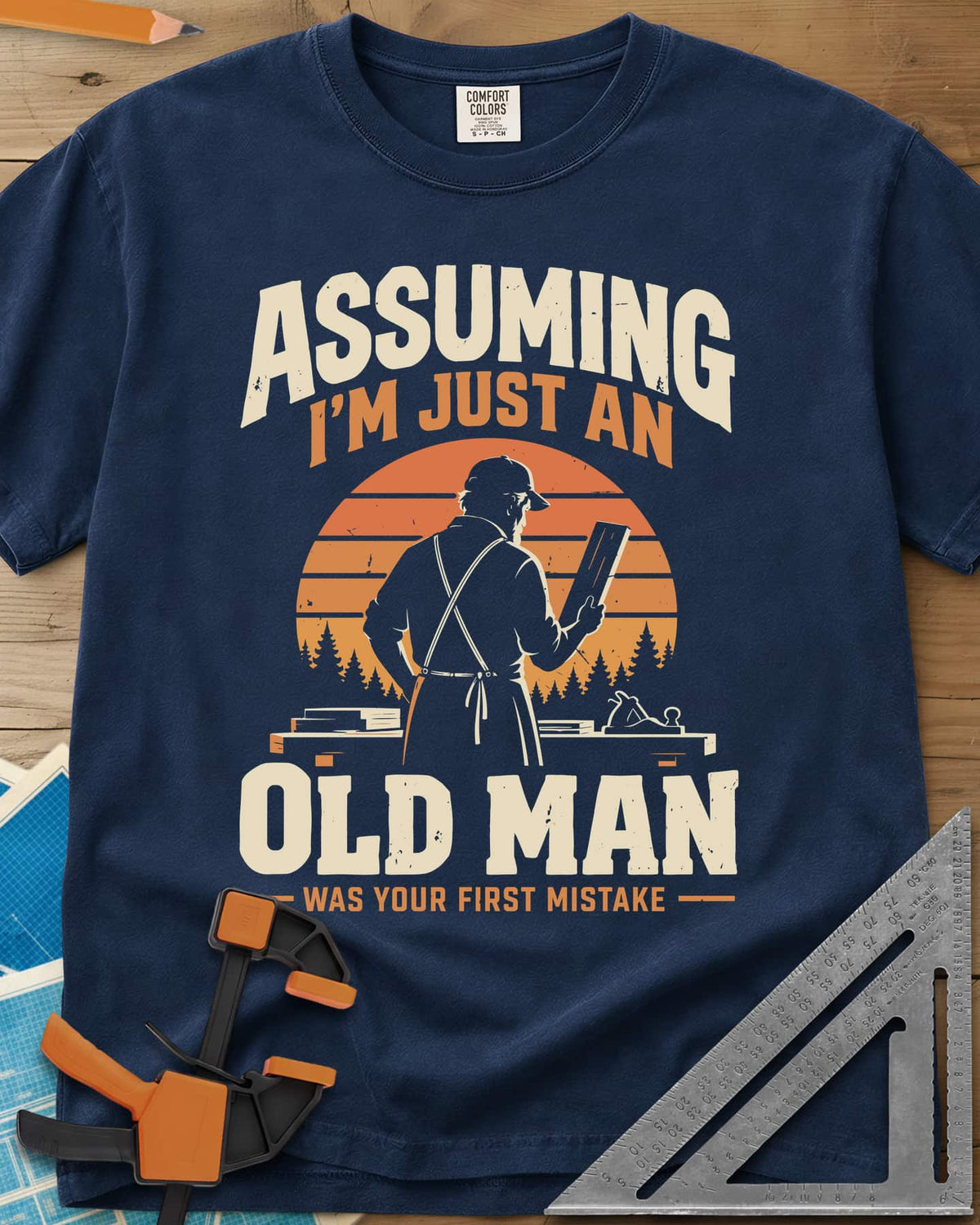 Old Man Mistake heavyweight tee in Navy, a woodworker in an apron holding a board before a striped sunset