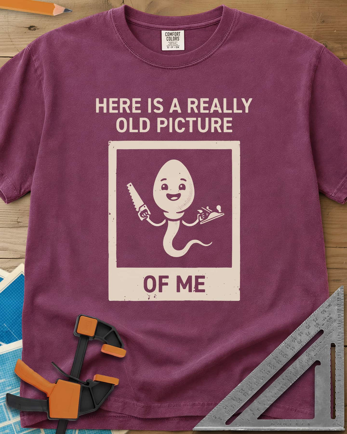 Old Picture heavyweight tee in Berry, a smiling cartoon figure with a long tail holding a saw and a plane