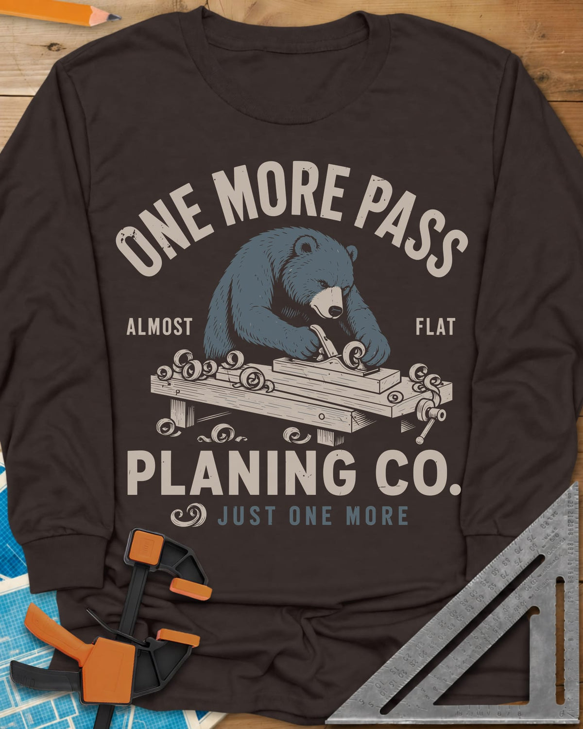 One More Pass long sleeve shirt in Dark Chocolate, a blue bear hand-planing a board at a workbench, shavings curling