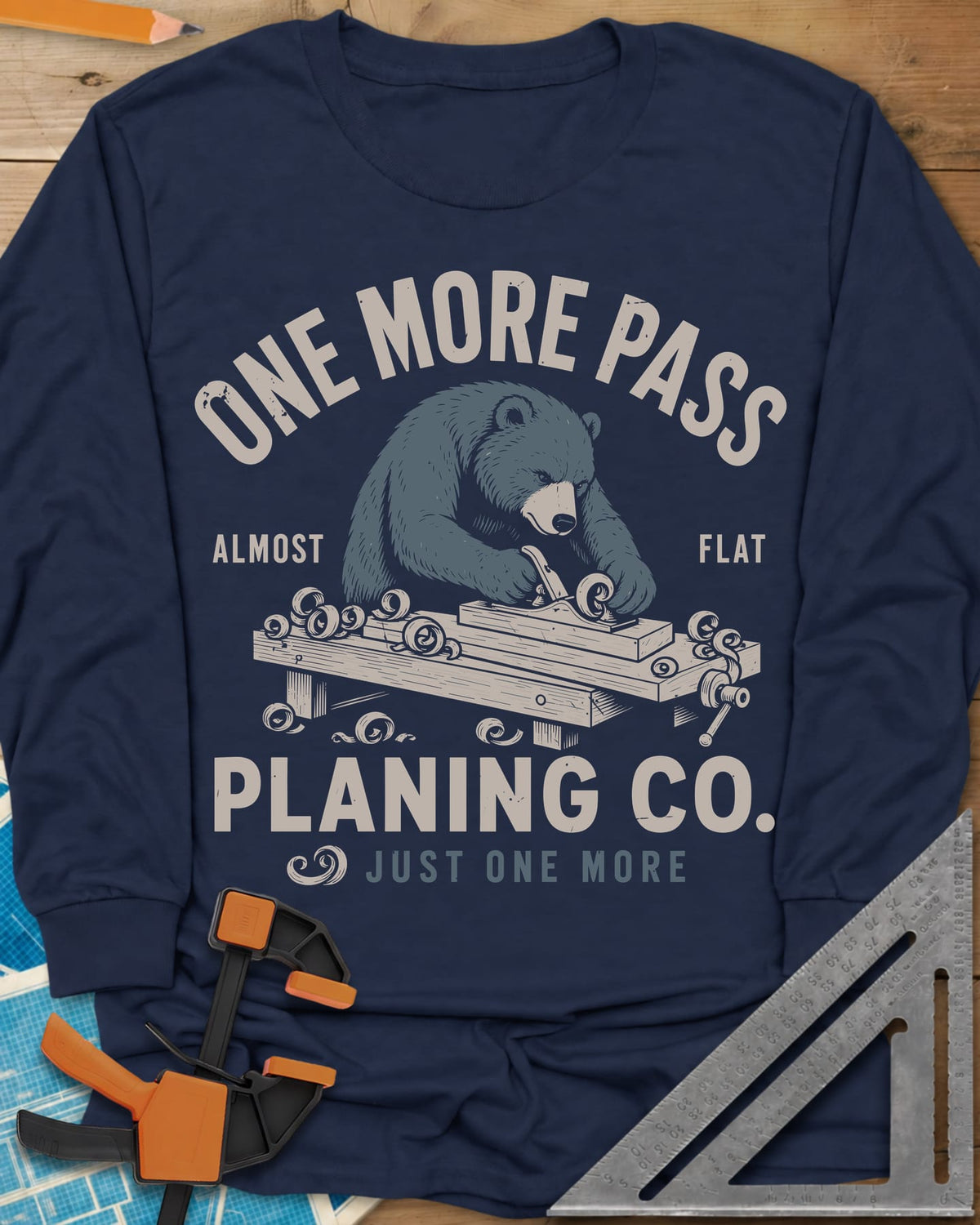 One More Pass long sleeve shirt in Navy, a blue bear hand-planing a board at a workbench, shavings curling