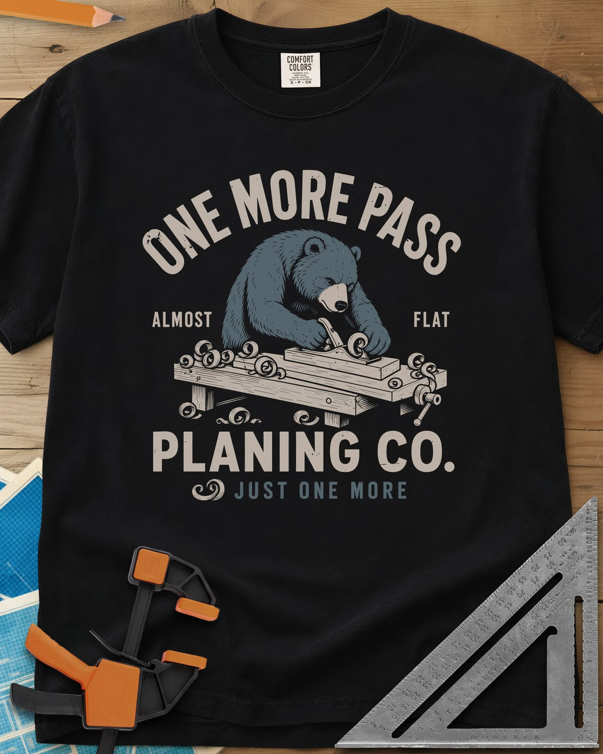 One More Pass heavyweight tee in Black, a blue bear hand-planing a board at a workbench, shavings curling