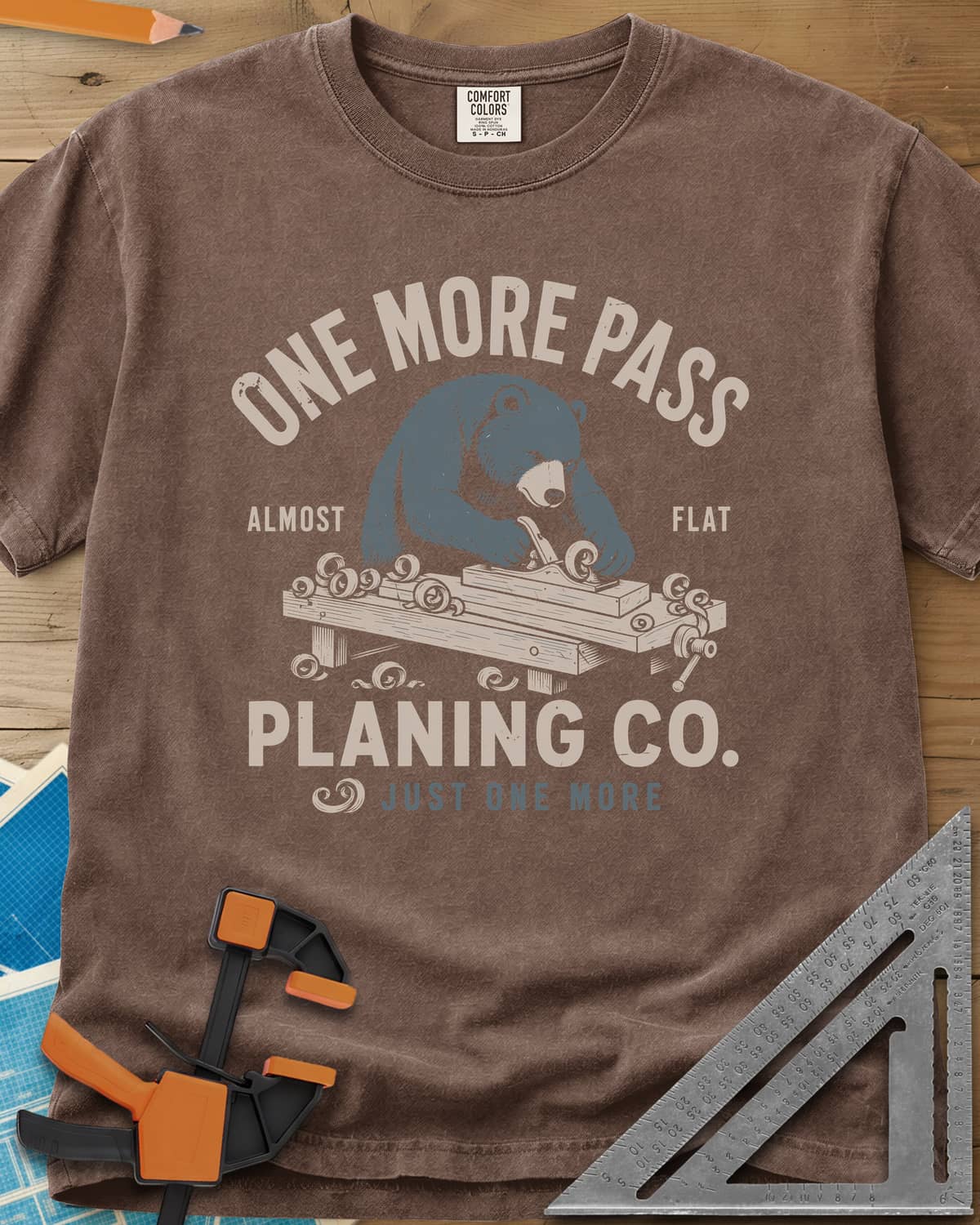 One More Pass heavyweight tee in Espresso, a blue bear hand-planing a board at a workbench, shavings curling