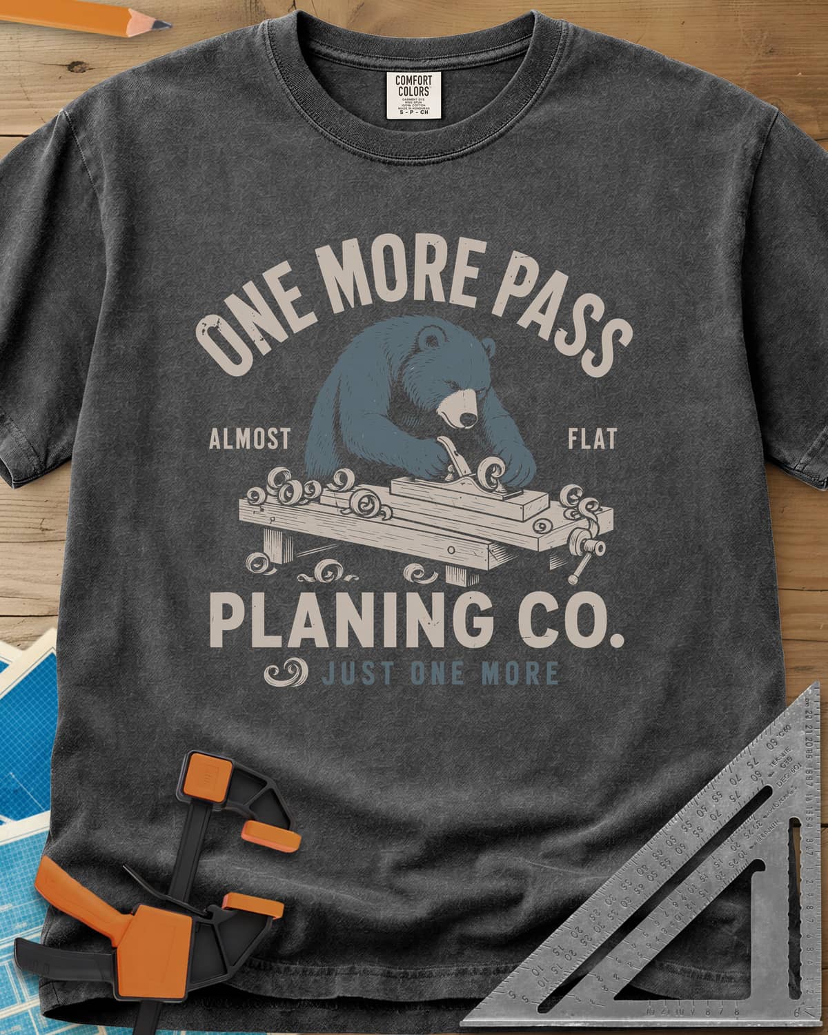 One More Pass heavyweight tee in Pepper, a blue bear hand-planing a board at a workbench, shavings curling