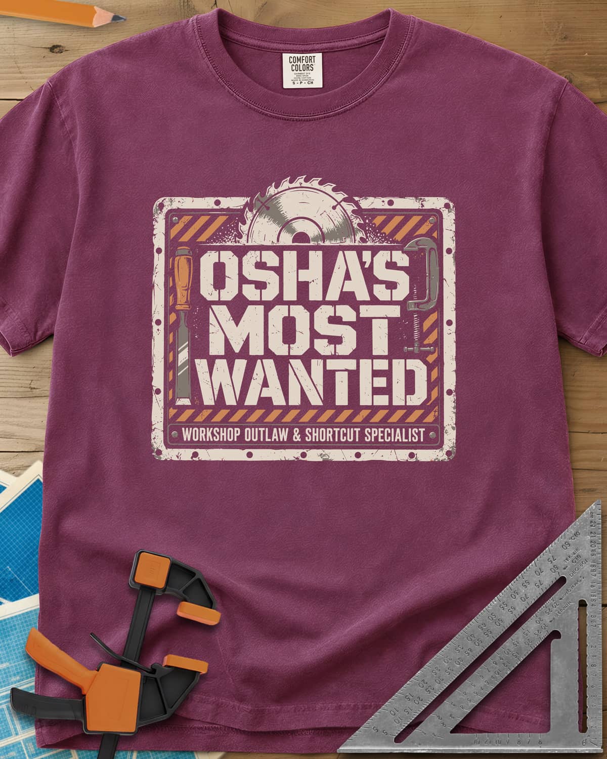 OSHA'S Most Wanted heavyweight tee in Berry, a saw blade, chisel and C-clamp around a hazard-striped plate