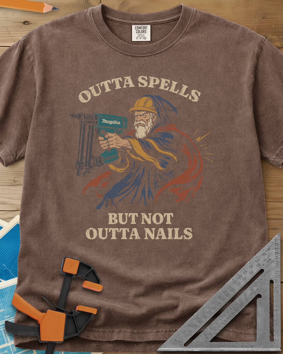 Outta Spells But Not Outta Nails heavyweight tee in Espresso, a bearded wizard in a hard hat aiming a teal nail gun