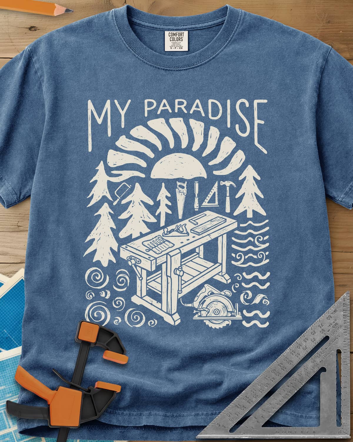 Paradise Workshop heavyweight tee in Blue Jean, linocut sun, pines, hand tools and a workbench with a plane