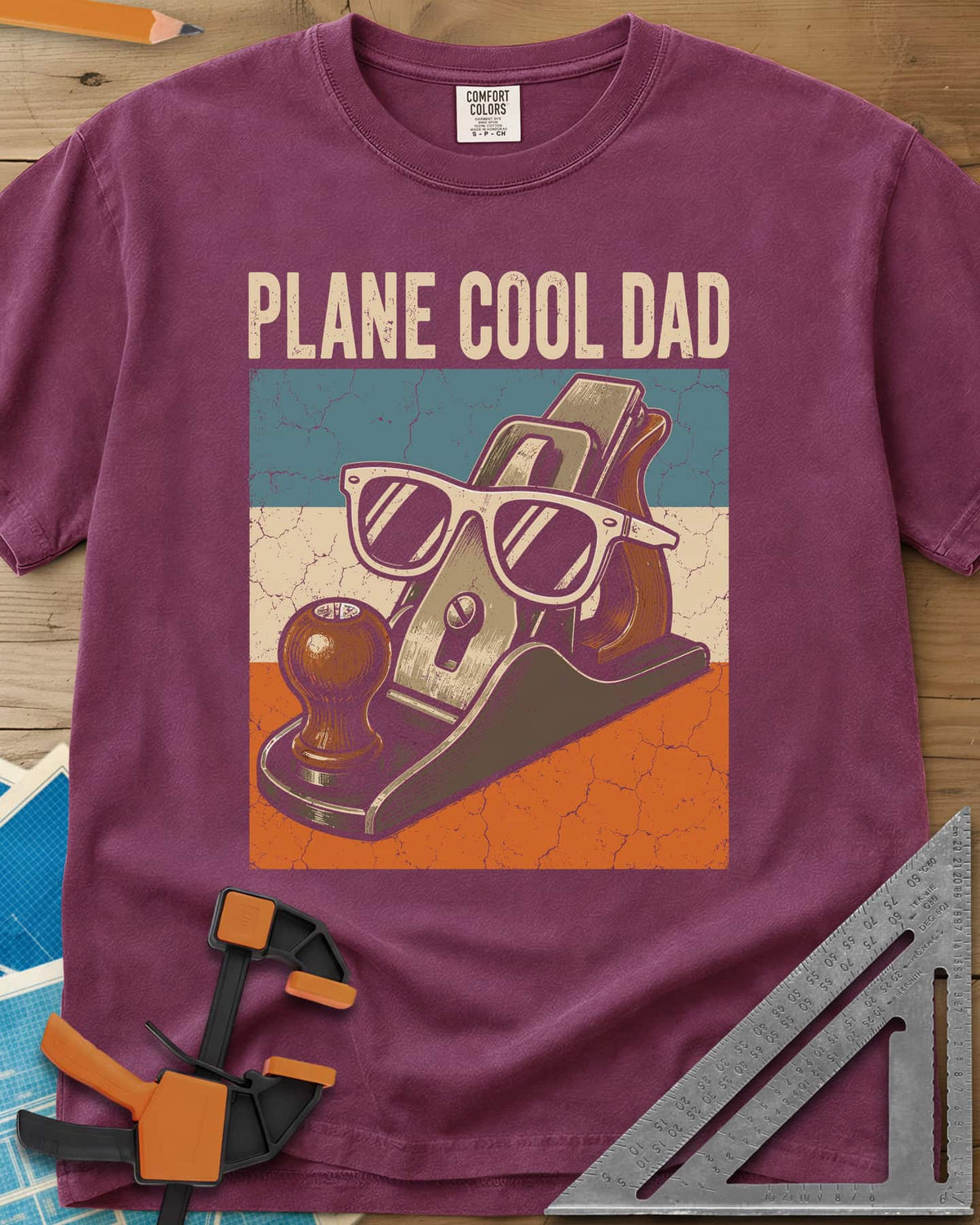 Plane Cool Dad heavyweight tee in Berry, a hand plane in white sunglasses on a retro striped panel