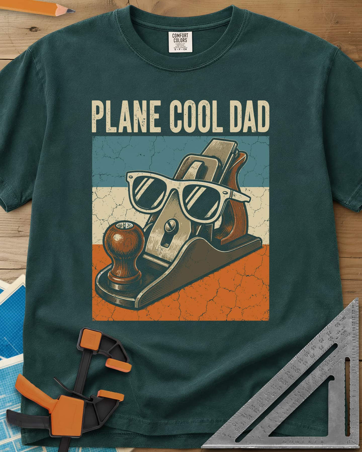 Plane Cool Dad heavyweight tee in Blue Spruce, a hand plane in white sunglasses on a retro striped panel