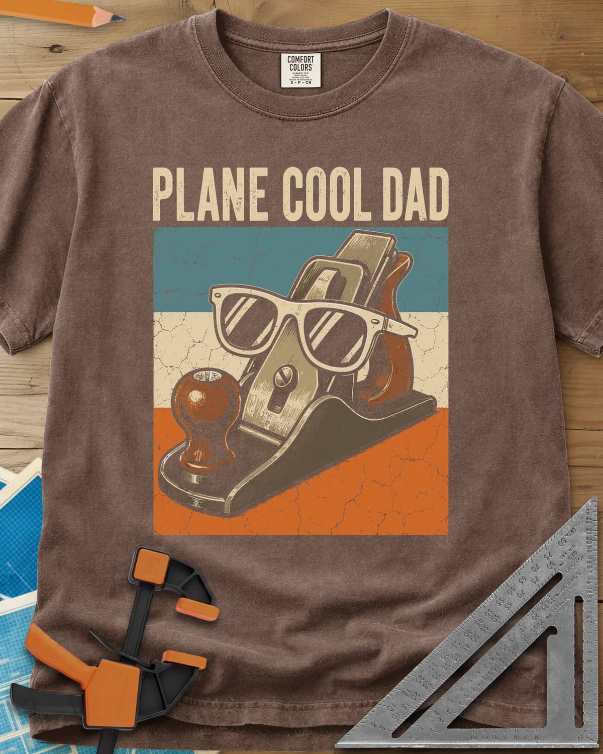 Plane Cool Dad heavyweight tee in Espresso, a hand plane in white sunglasses on a retro striped panel