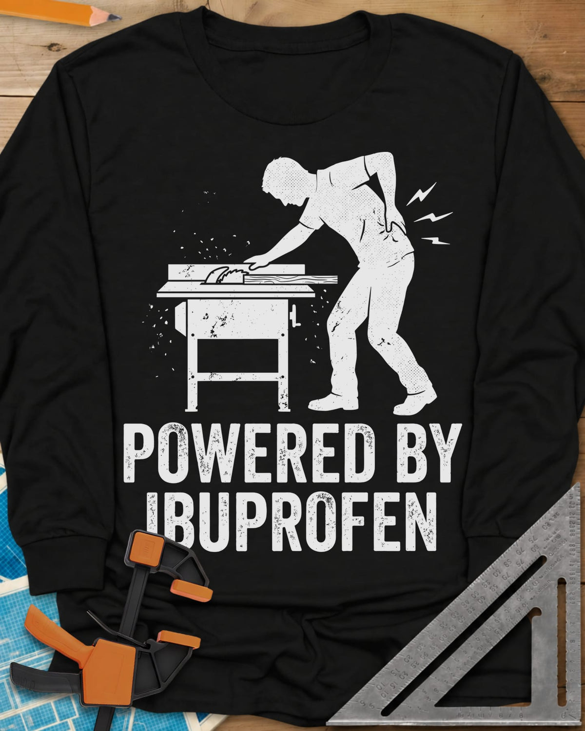 Powered By Ibuprofen long sleeve shirt in Black, a man at a table saw with a hand on his sore back