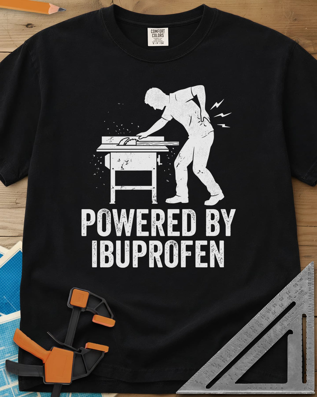 Powered By Ibuprofen heavyweight tee in Black, a man at a table saw with a hand on his sore back