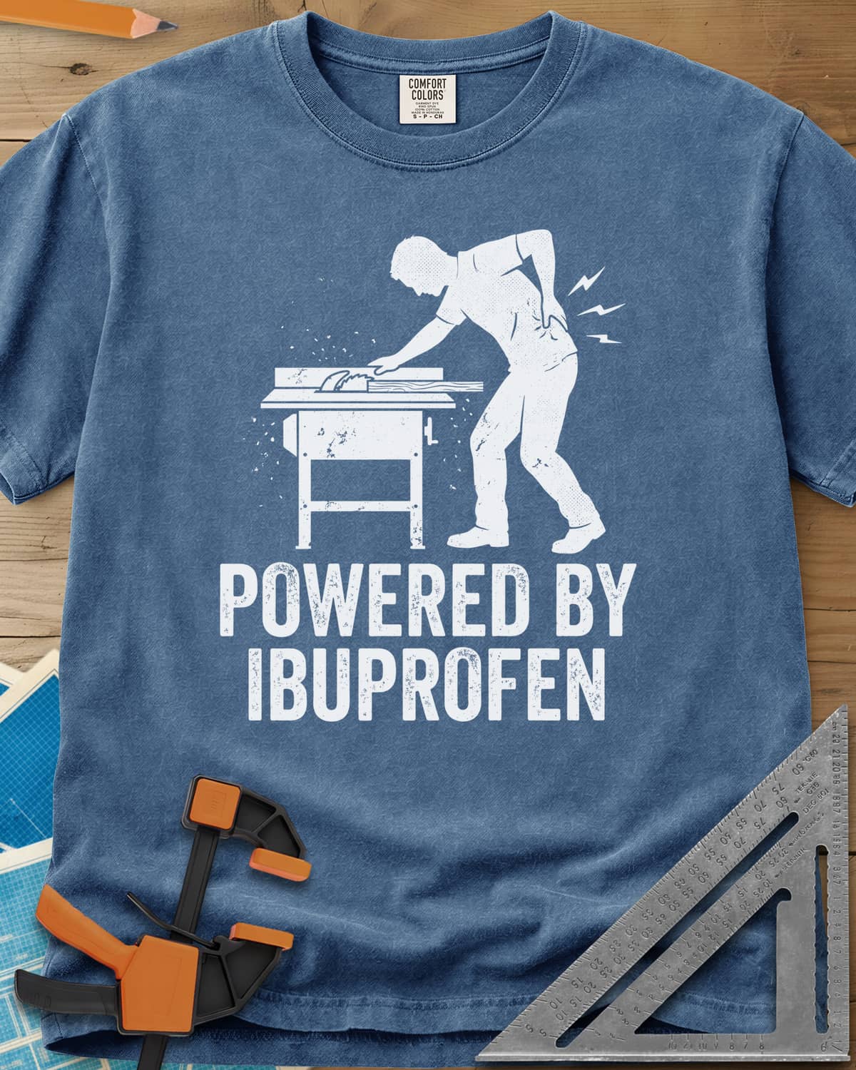 Powered By Ibuprofen heavyweight tee in Blue Jean, a man at a table saw with a hand on his sore back