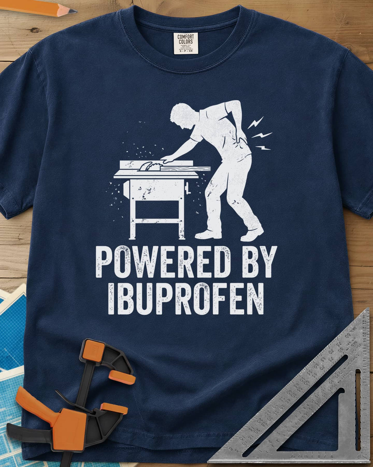 Powered By Ibuprofen heavyweight tee in Navy, a man at a table saw with a hand on his sore back