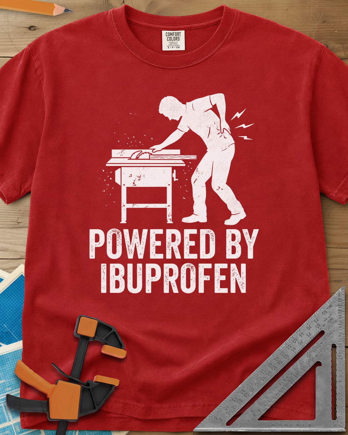 Powered By Ibuprofen heavyweight tee in Red, a man at a table saw with a hand on his sore back