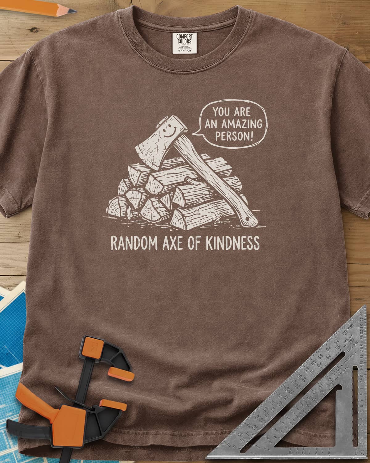 Random Axe of Kindness heavyweight tee in Espresso, a smiling axe on a woodpile with an encouraging speech bubble