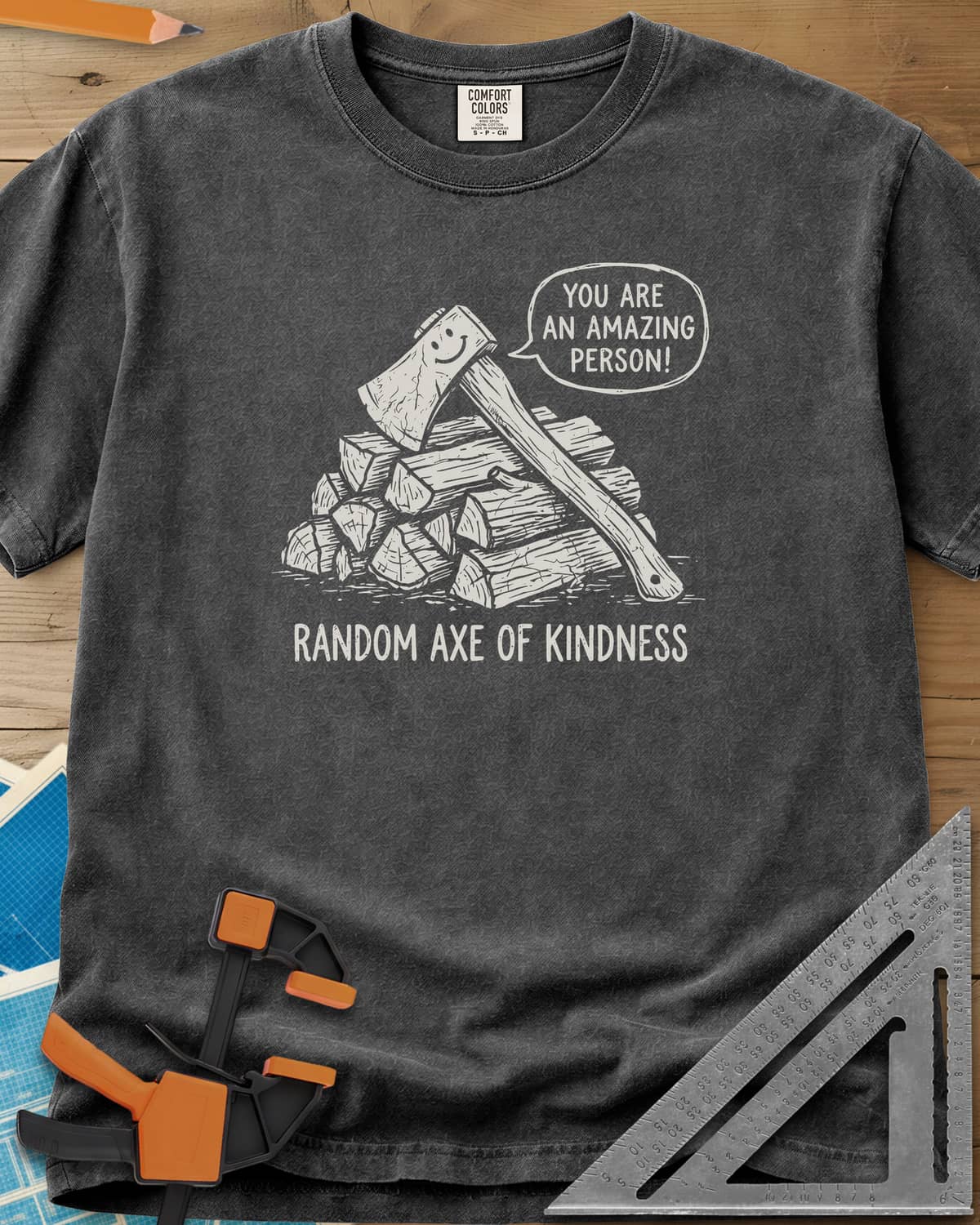 Random Axe of Kindness heavyweight tee in Pepper, a smiling axe on a woodpile with an encouraging speech bubble