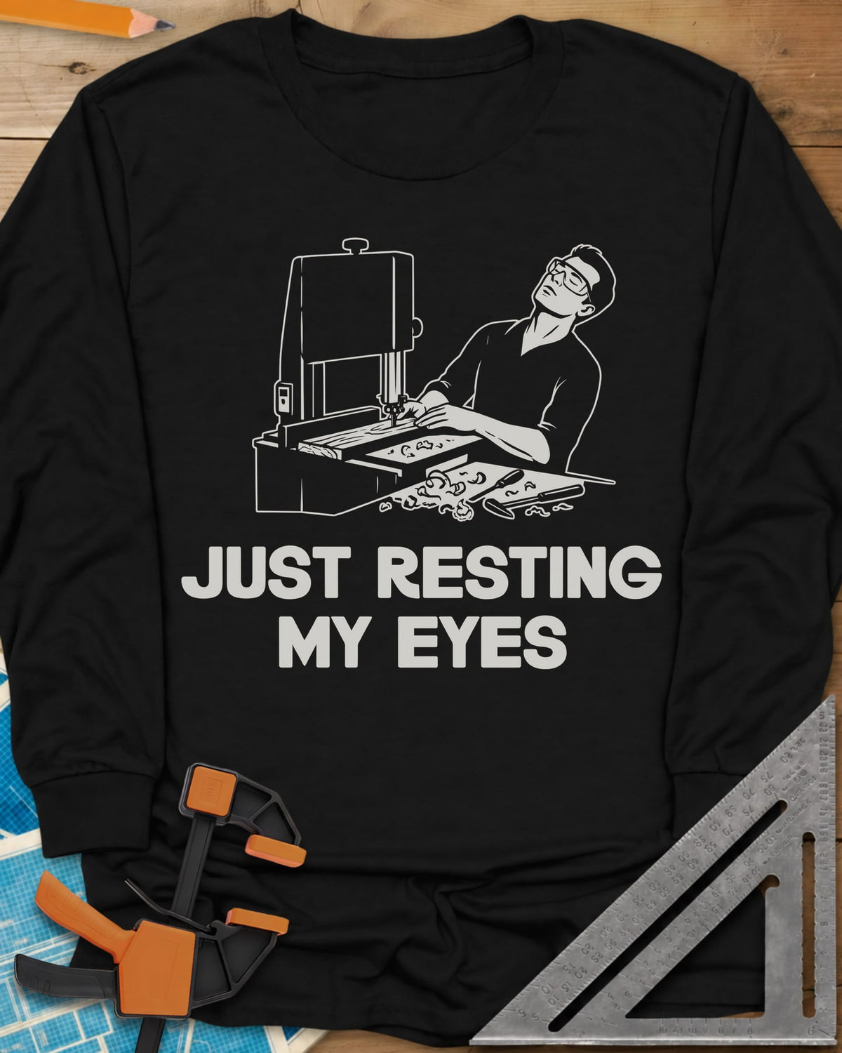 Resting My Eyes long sleeve shirt in Black, man in safety glasses tipped back at a band saw, shavings on the bench