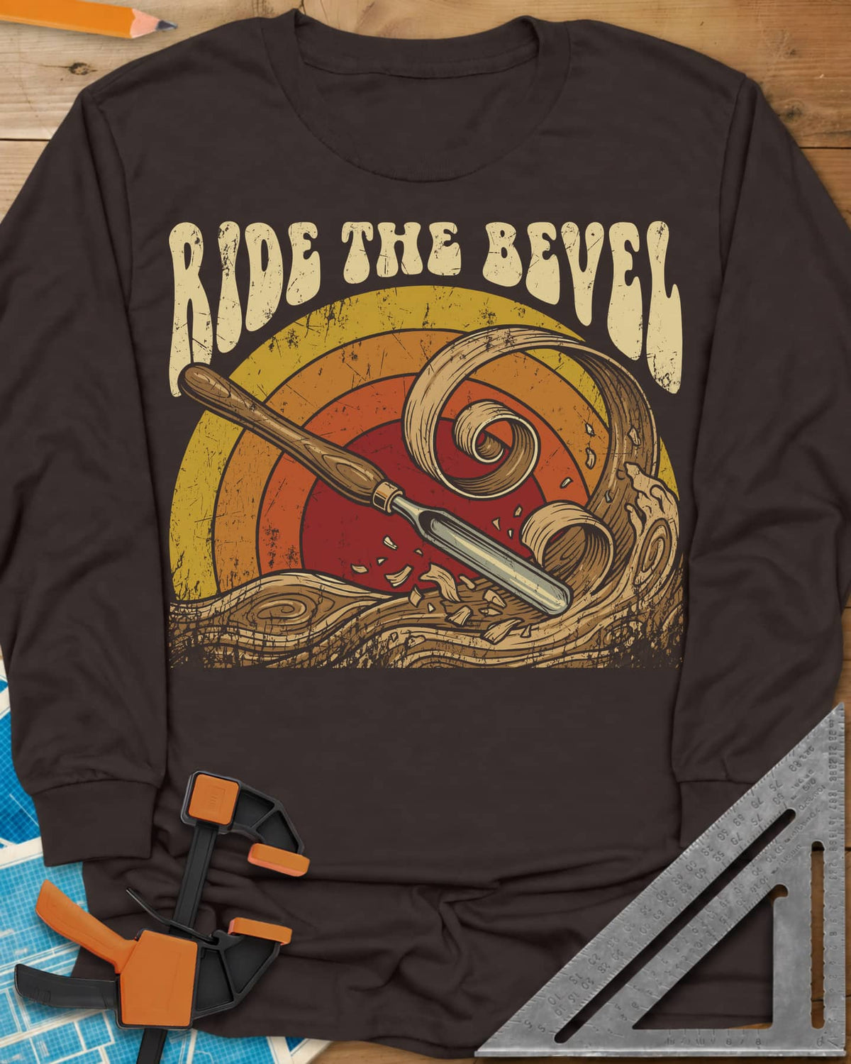 Ride The Bevel long sleeve shirt in Dark Chocolate, a carving gouge riding a wave of wood curls under a retro sunset