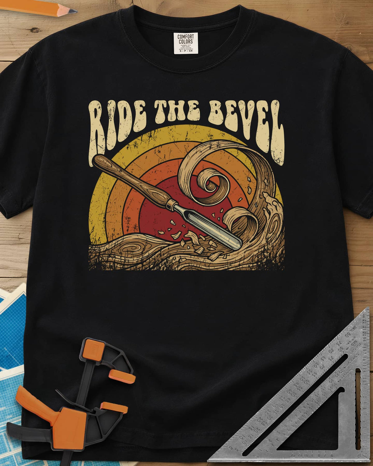 Ride The Bevel heavyweight tee in Black, a carving gouge riding a wave of wood curls under a retro sunset