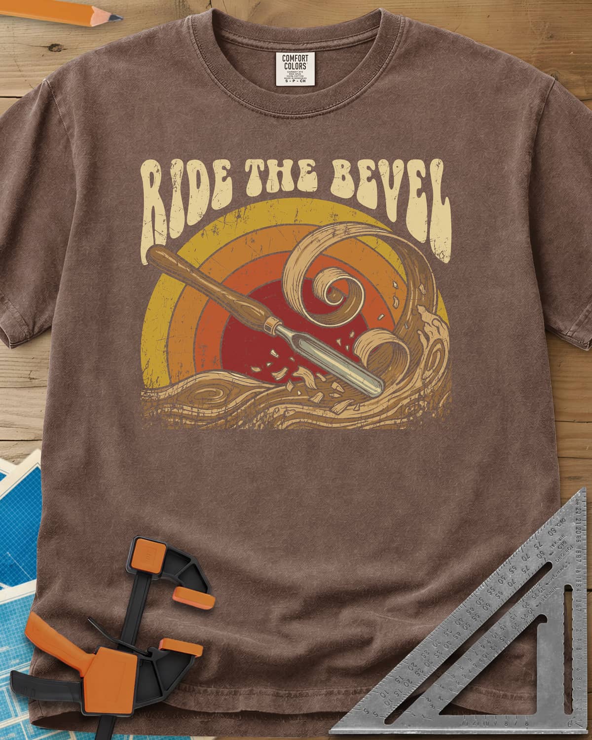 Ride The Bevel heavyweight tee in Espresso, a carving gouge riding a wave of wood curls under a retro sunset