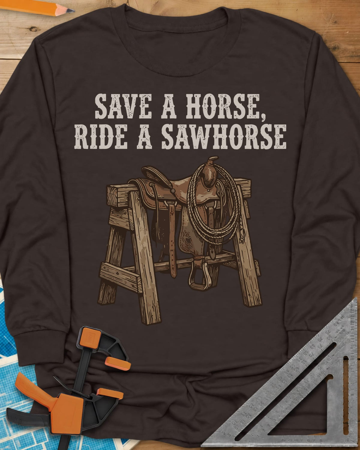 Save a Horse long sleeve shirt in Dark Chocolate, a western saddle and lasso rope draped over a wooden sawhorse