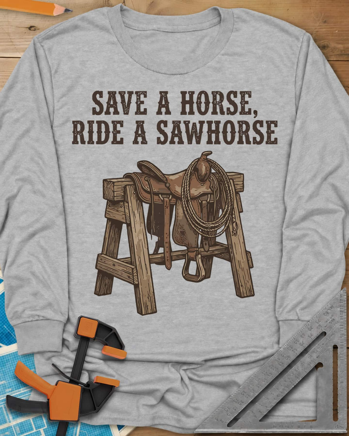 Save a Horse long sleeve shirt in Sport Grey, a western saddle and lasso rope draped over a wooden sawhorse
