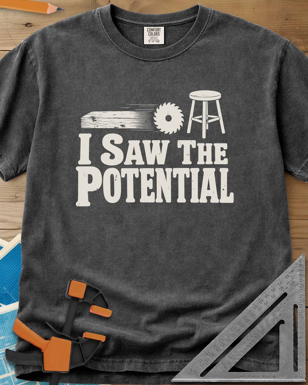 Saw The Potential heavyweight tee in Pepper, a speeding plank, a saw blade and a finished stool