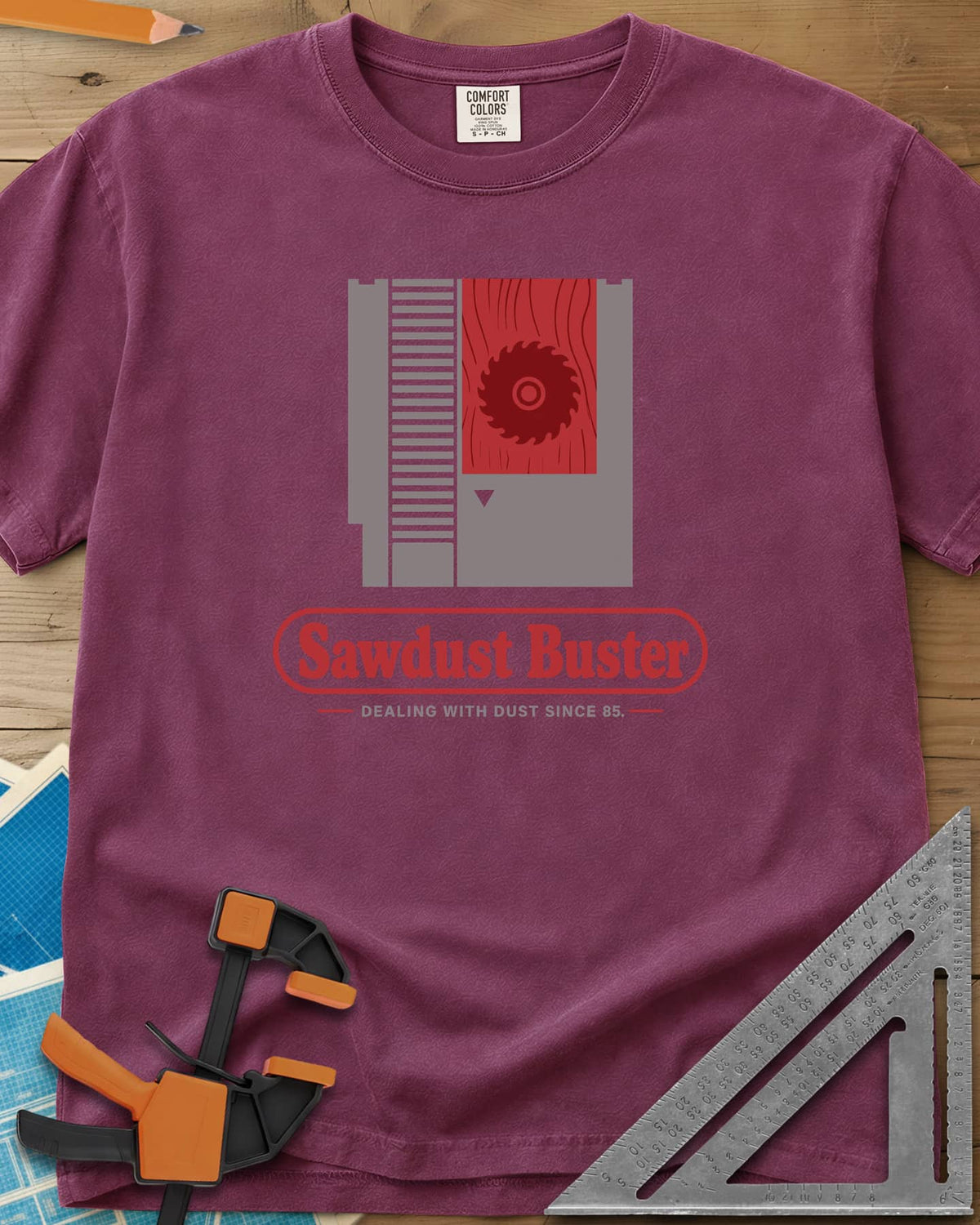 Sawdust Buster heavyweight tee in Berry, retro game cartridge with a saw blade on a red wood-grain label