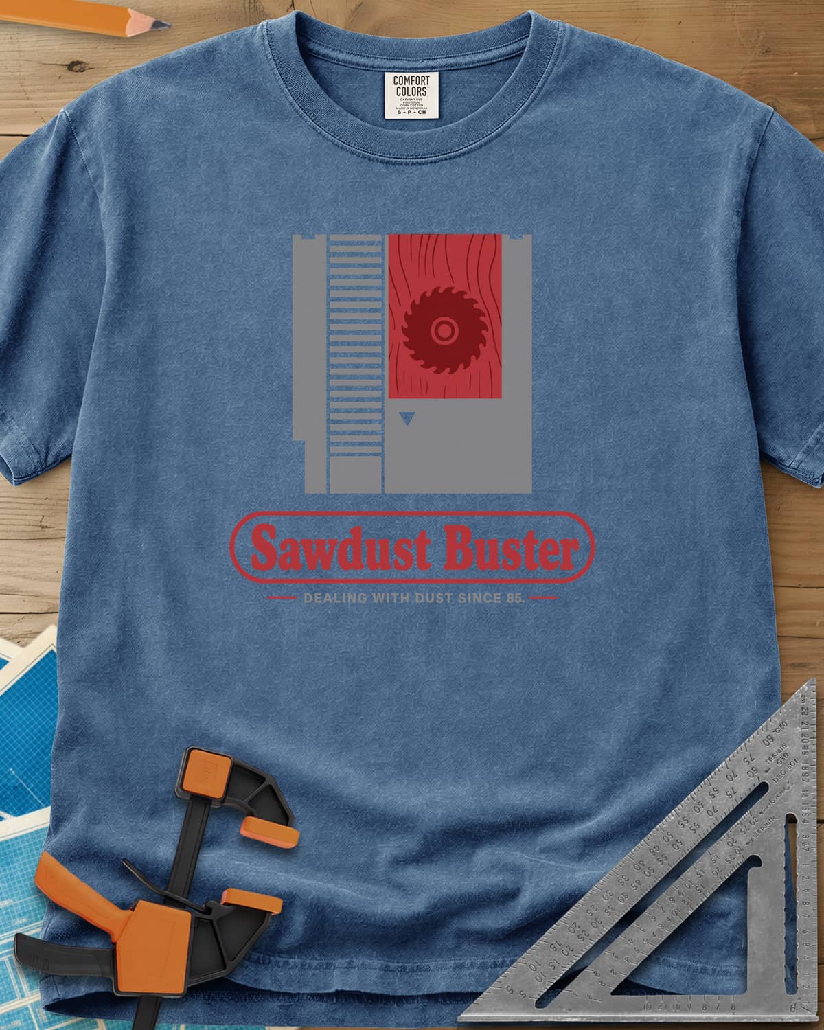 Sawdust Buster heavyweight tee in Blue Jean, retro game cartridge with a saw blade on a red wood-grain label
