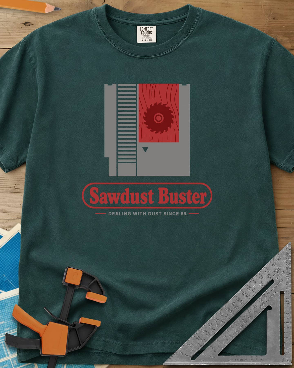 Sawdust Buster heavyweight tee in Blue Spruce, retro game cartridge with a saw blade on a red wood-grain label