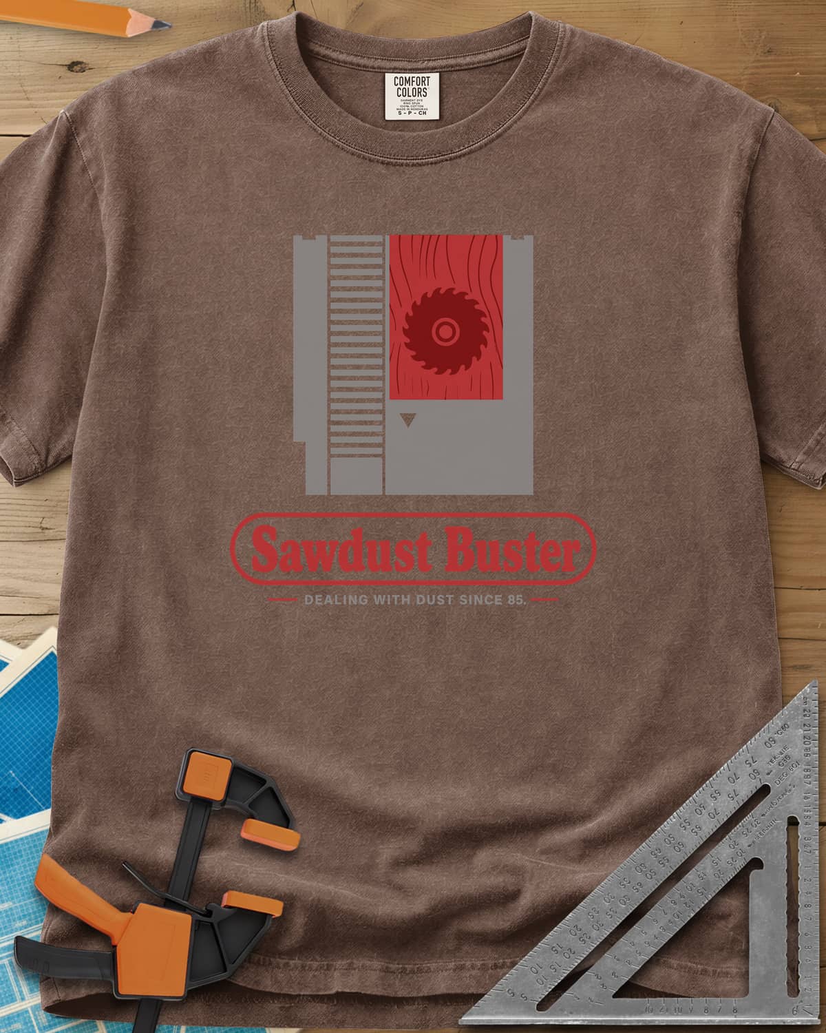 Sawdust Buster heavyweight tee in Espresso, retro game cartridge with a saw blade on a red wood-grain label