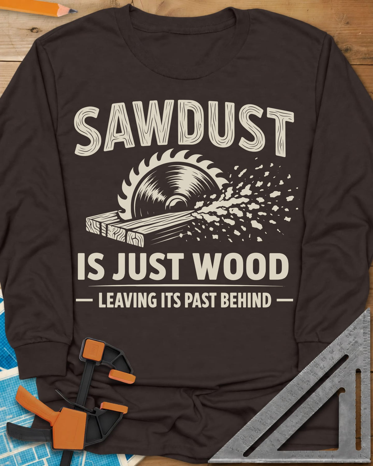Sawdust Leaving Its Past Behind long sleeve shirt in Dark Chocolate, wood-grain lettering above a circular saw cutting a