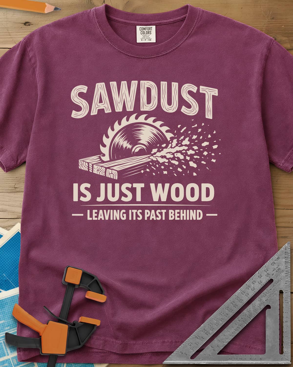 Sawdust Leaving Its Past Behind heavyweight tee in Berry, wood-grain lettering above a circular saw cutting a board