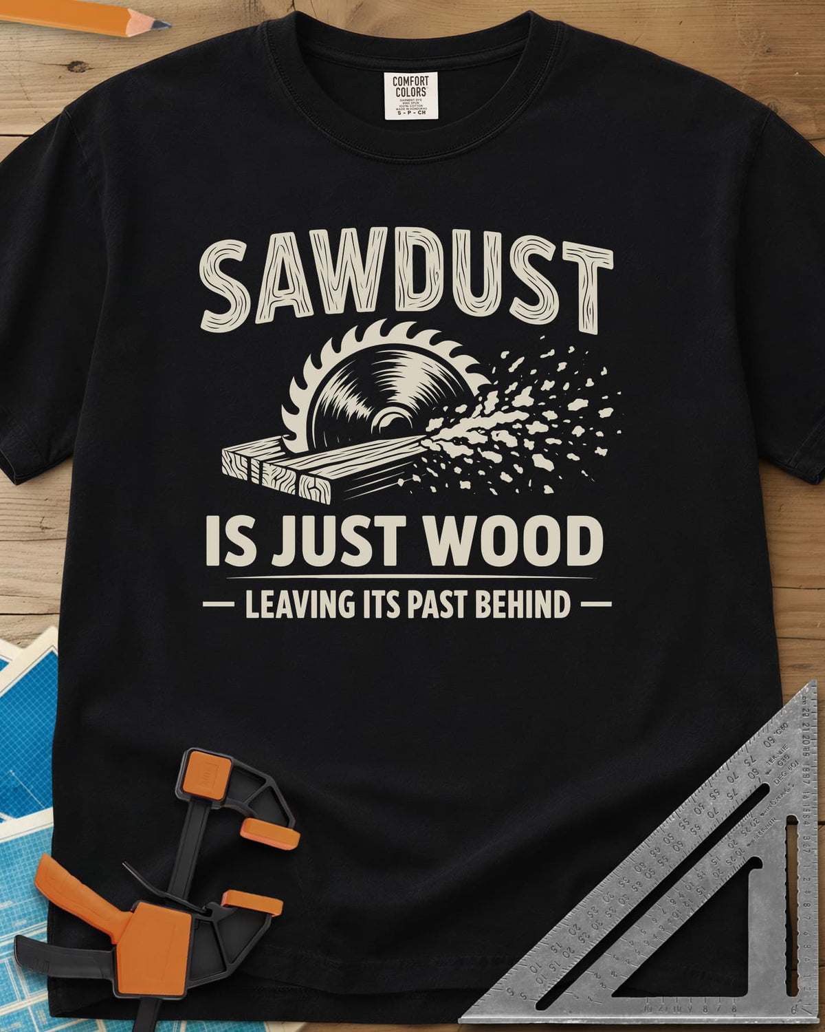 Sawdust Leaving Its Past Behind heavyweight tee in Black, wood-grain lettering above a circular saw cutting a board