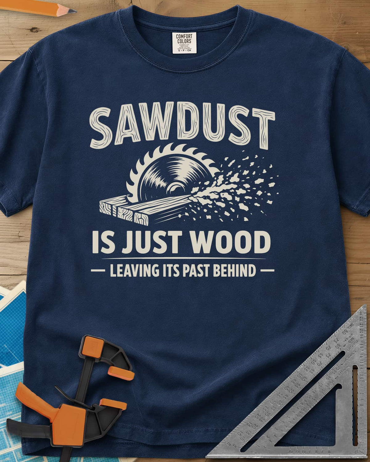Sawdust Leaving Its Past Behind heavyweight tee in Navy, wood-grain lettering above a circular saw cutting a board