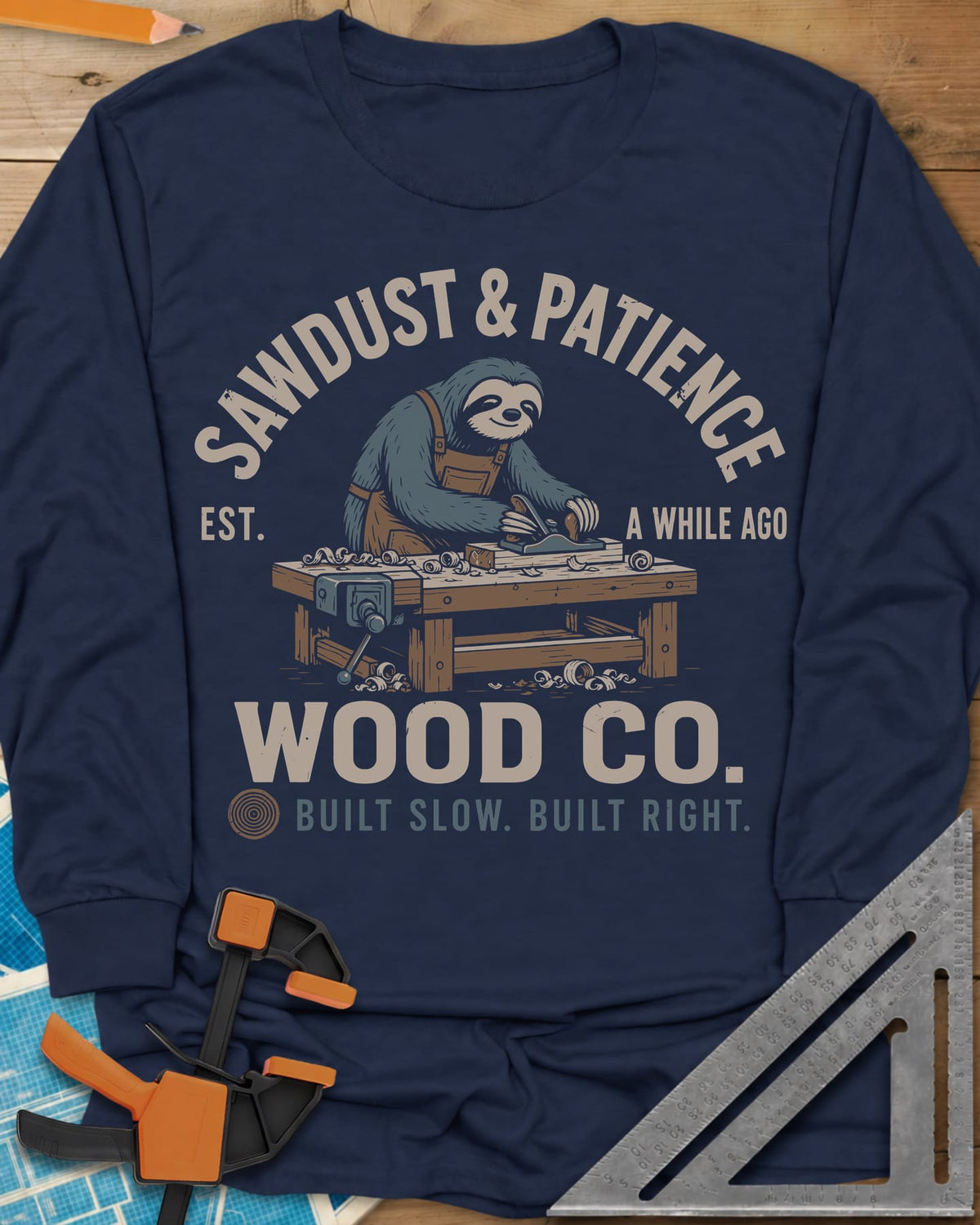 Sawdust & Patience long sleeve shirt in Navy, a sloth in an apron planing wood at a bench with a vise