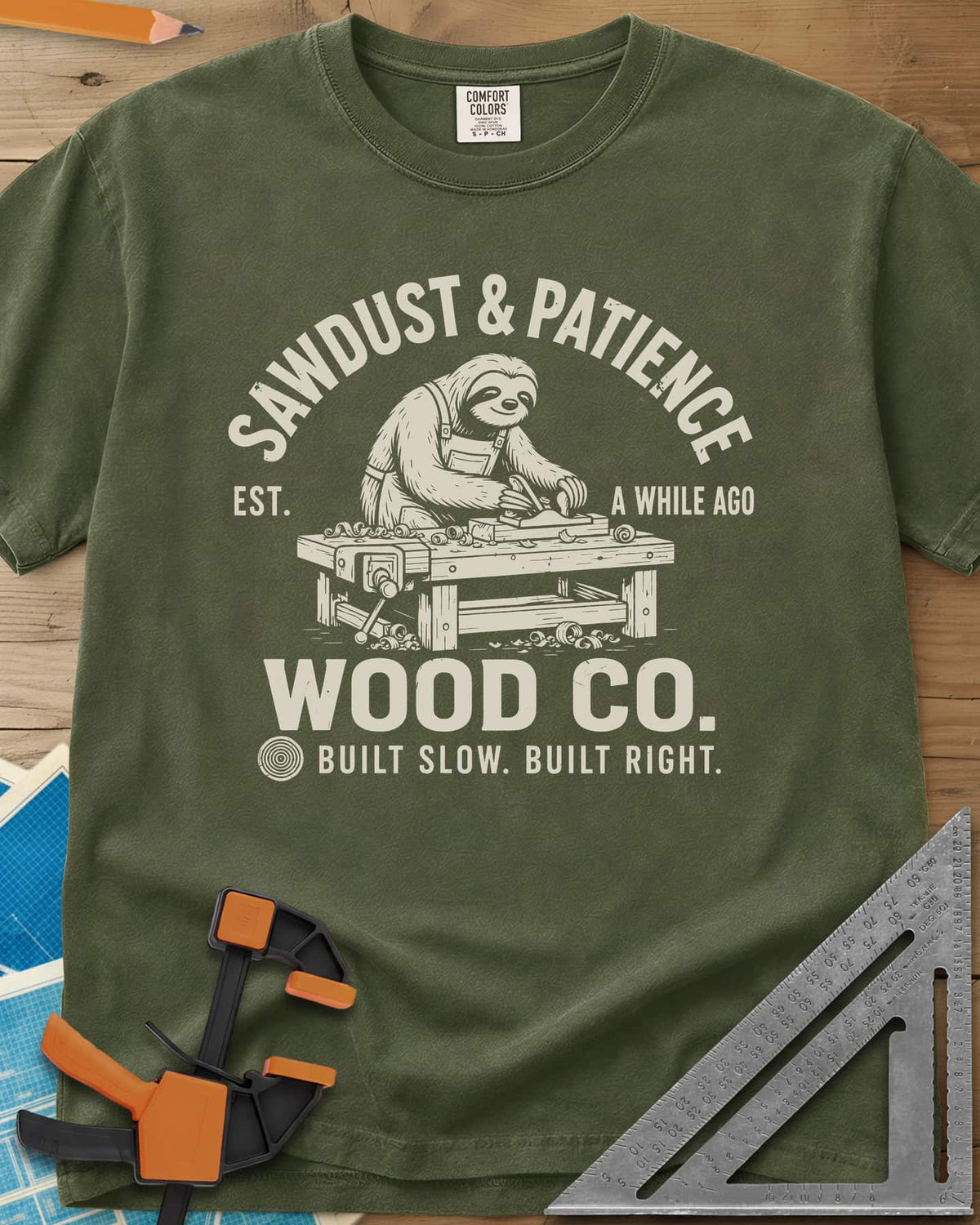 Sawdust & Patience heavyweight tee in Hemp, a sloth in an apron planing wood at a bench with a vise