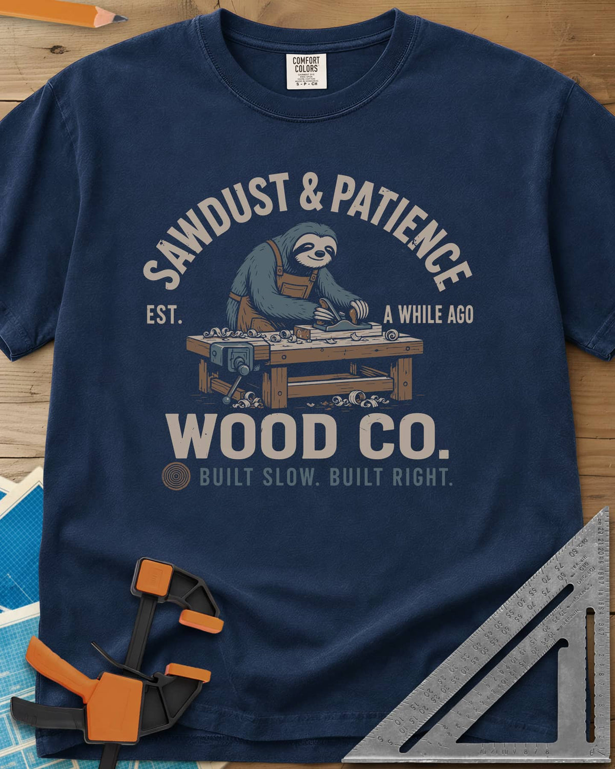 Sawdust & Patience heavyweight tee in Navy, a sloth in an apron planing wood at a bench with a vise