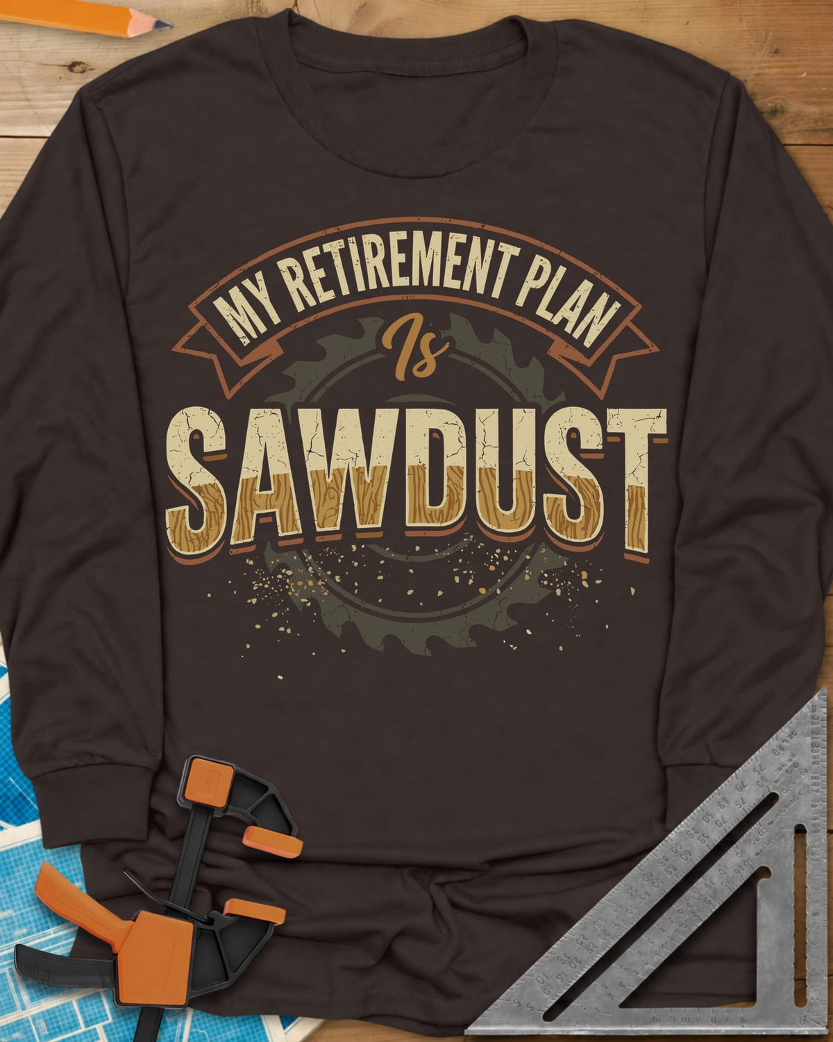 Sawdust Retirement long sleeve shirt in Dark Chocolate, a ribbon banner over a saw blade, cracked wood-grain letters