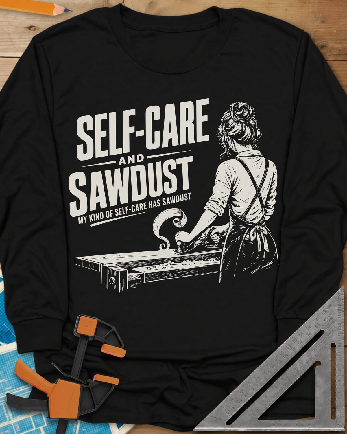 Self-Care & Sawdust long sleeve shirt in Black, a woman at a workbench running a hand plane, shaving curling up