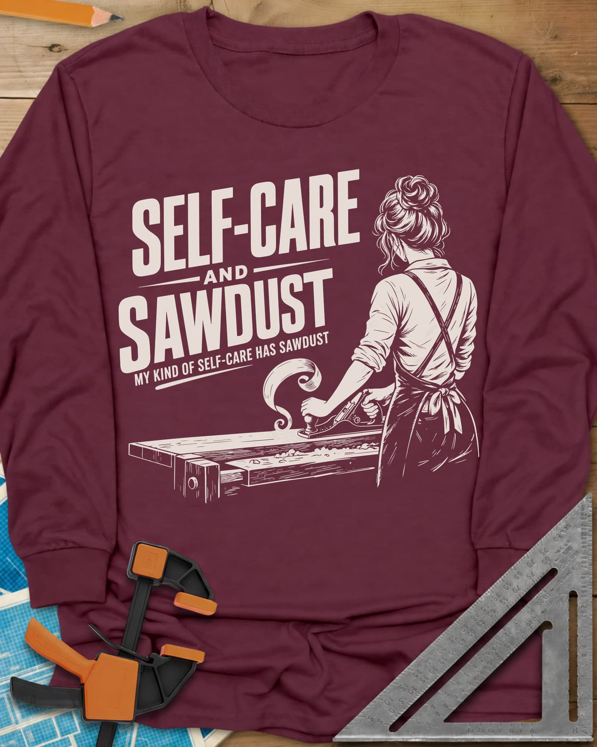 Self-Care & Sawdust long sleeve shirt in Maroon, a woman at a workbench running a hand plane, shaving curling up