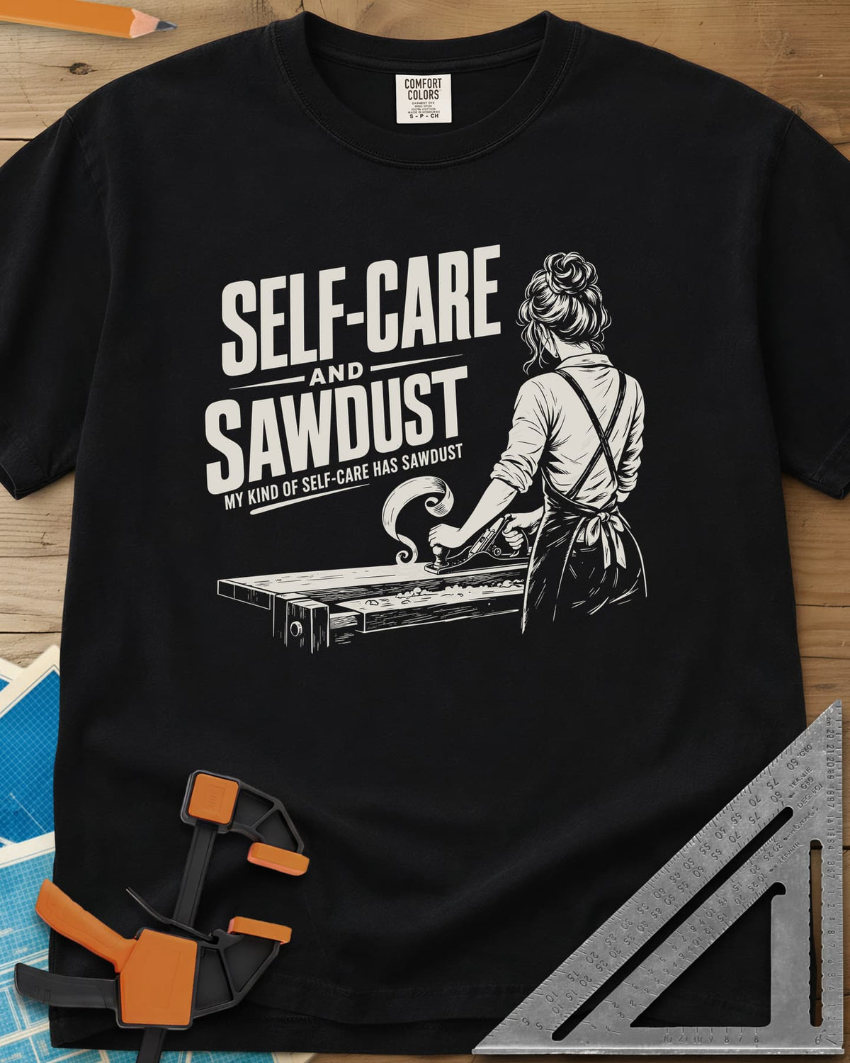 Self-Care & Sawdust heavyweight tee in Black, a woman at a workbench running a hand plane, shaving curling up