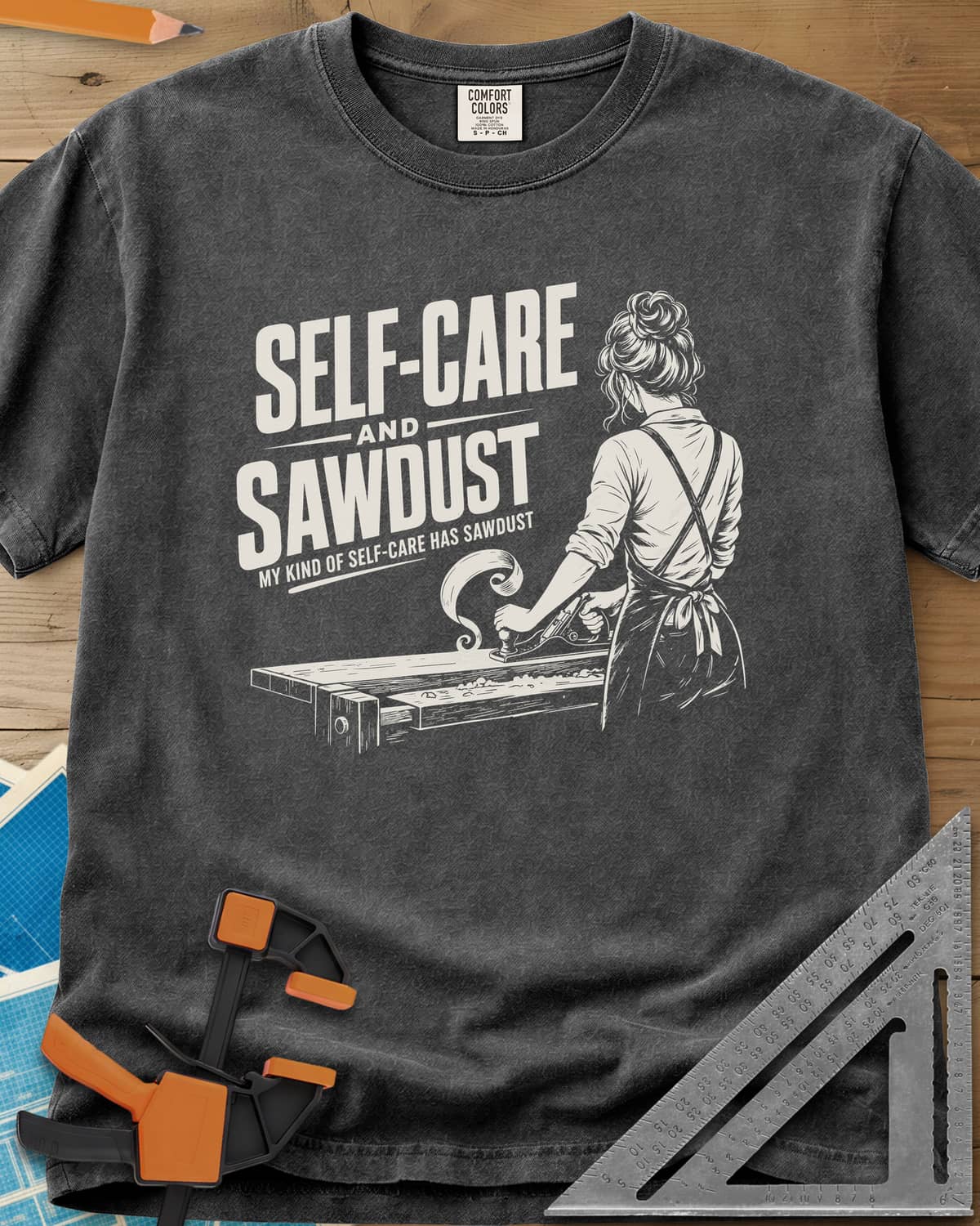 Self-Care & Sawdust heavyweight tee in Pepper, a woman at a workbench running a hand plane, shaving curling up
