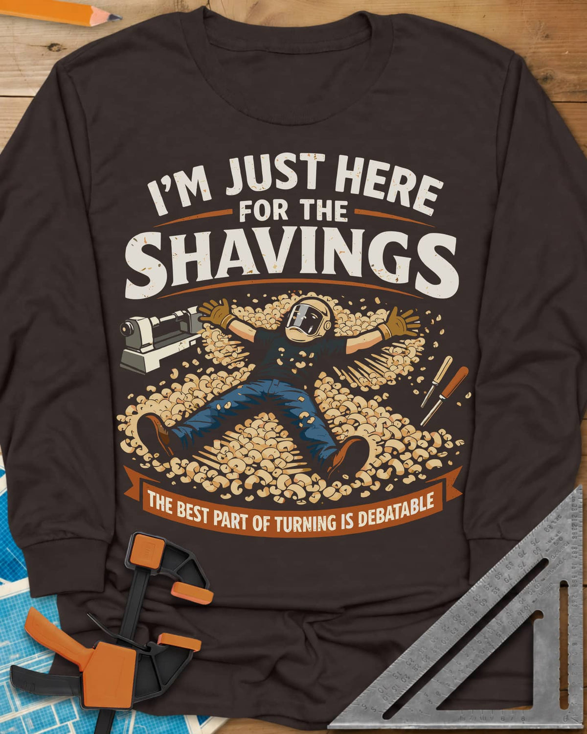 Shavings long sleeve shirt in Dark Chocolate, a turner in a face shield lying in a drift of wood shavings
