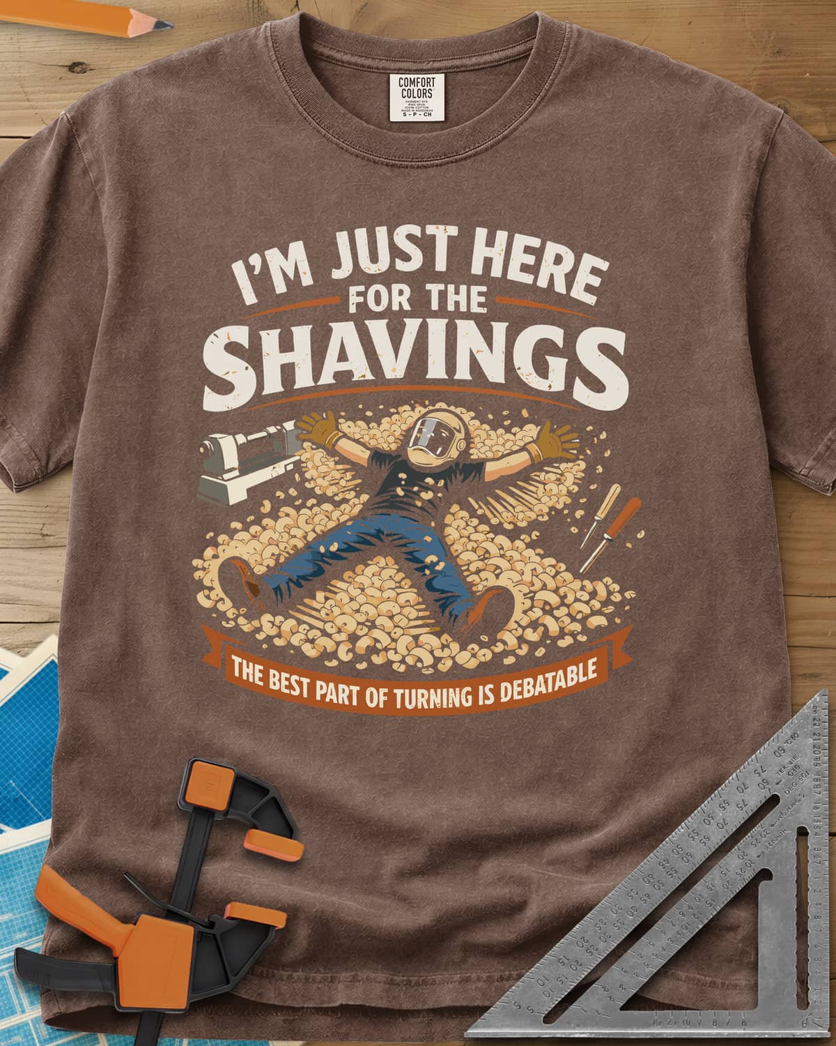Shavings heavyweight tee in Espresso, a turner in a face shield lying in a drift of wood shavings