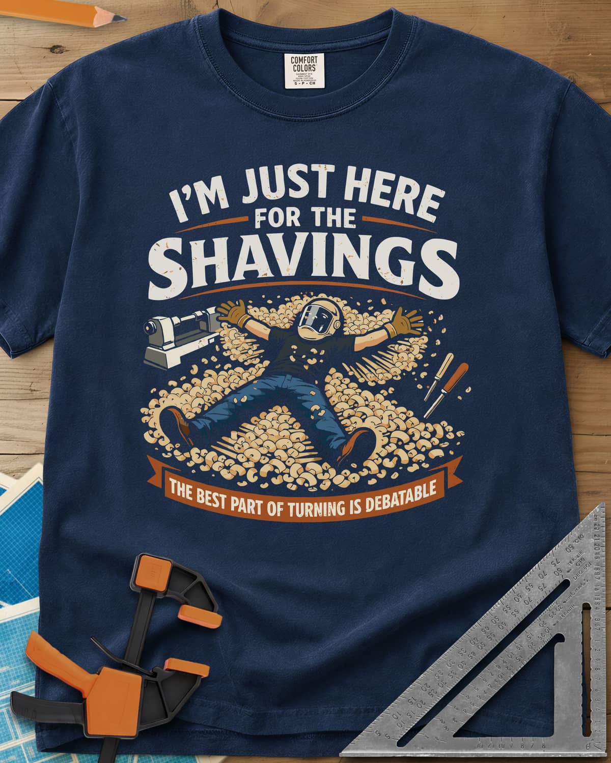 Shavings heavyweight tee in Navy, a turner in a face shield lying in a drift of wood shavings