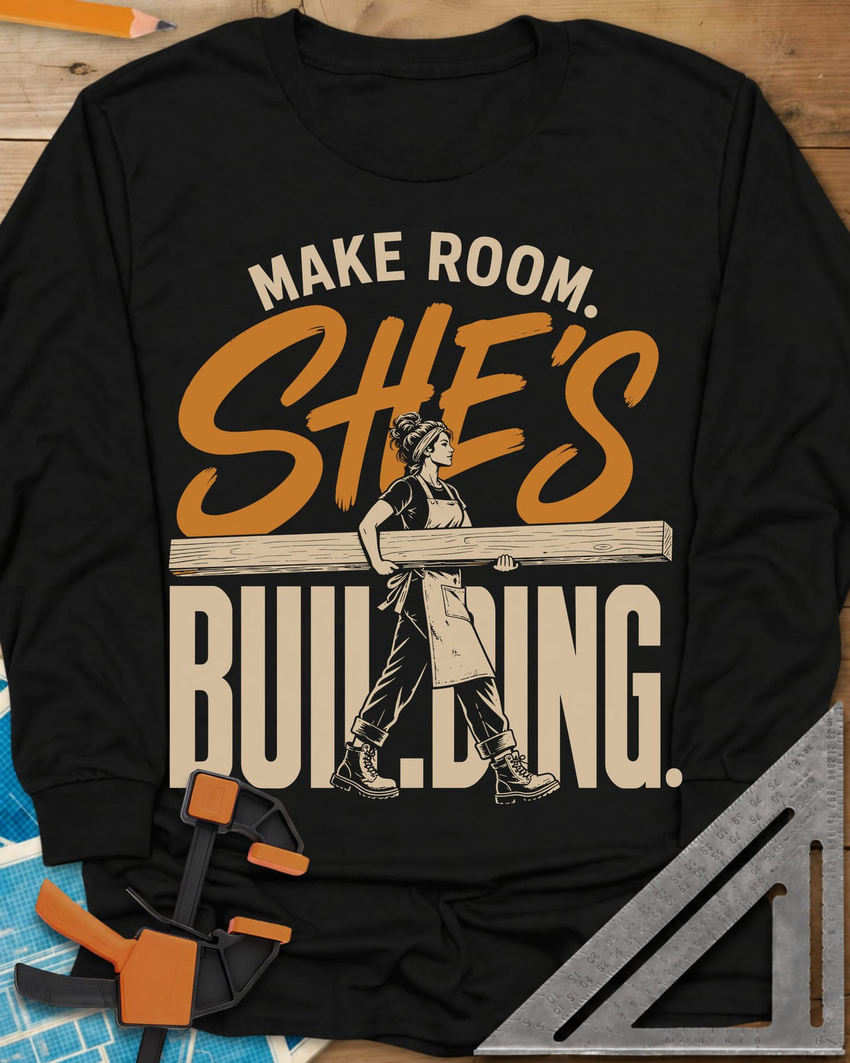 She'S Building long sleeve shirt in Black, a woman in boots carrying a long beam through the lettering