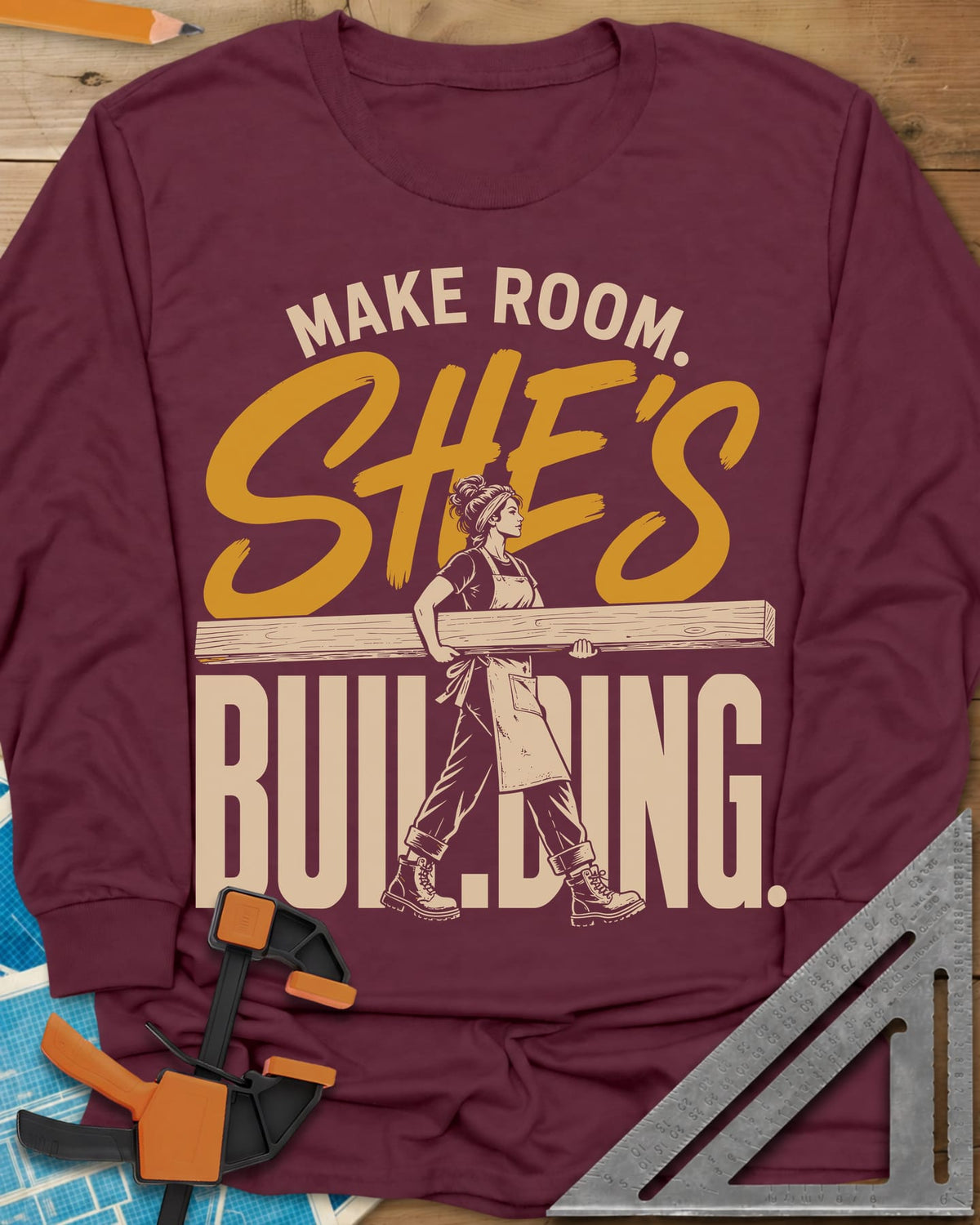 She'S Building long sleeve shirt in Maroon, a woman in boots carrying a long beam through the lettering