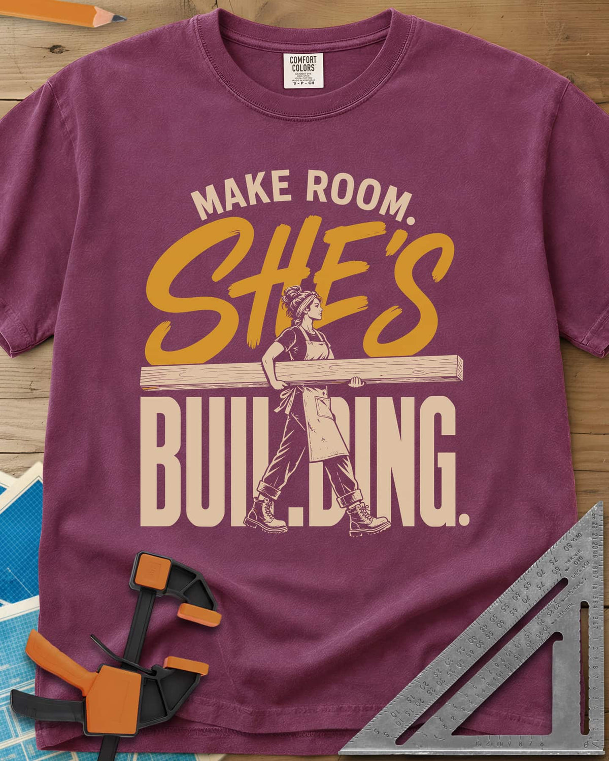 She'S Building heavyweight tee in Berry, a woman in boots carrying a long beam through the lettering